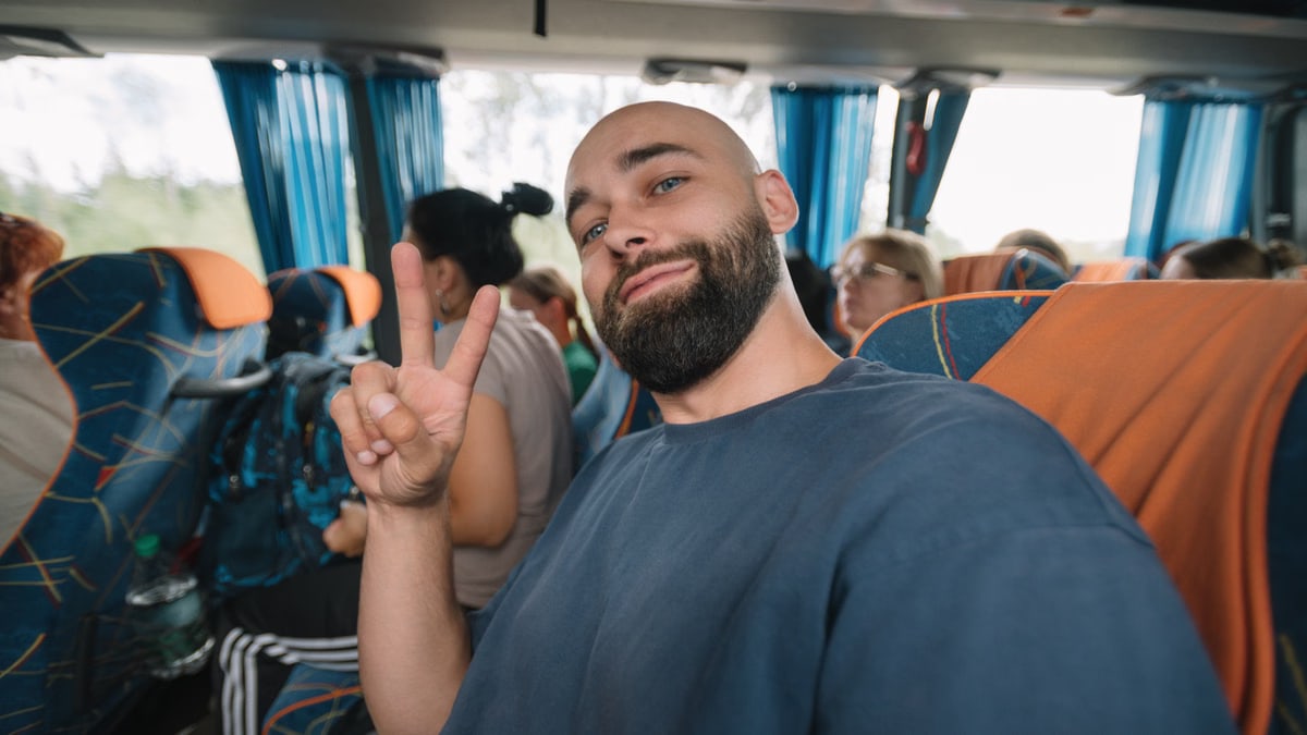 A man giving a peace sign while sitting in a bus with other passengers.